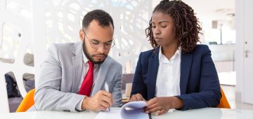 Businessman and businesswoman signing contract. Young African American business colleagues sitting in office and working with papers. Paperwork concept